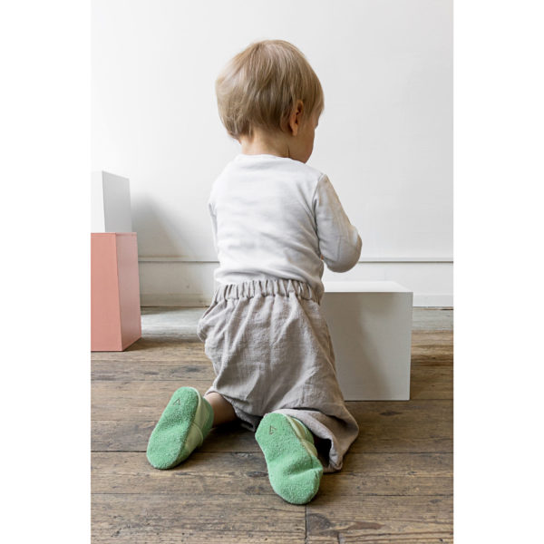 Kind kniet auf Holzboden und trägt Krabbelschuhe MOQ aus Naturleder in hellgrün