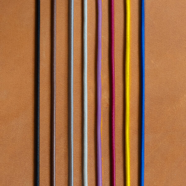 Gummibänder für Notizbuchhüllen in den Farben Schwarz, Braun, Grau, Creme, Rot, Gelb und Blau auf cognacfarbenem Naturleder.