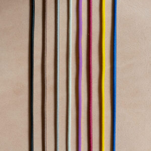 Gummibänder für Notizbuchhüllen in den Farben Schwarz, Braun, Grau, Creme, Rot, Gelb und Blau auf hellbraunem, Naturleder.