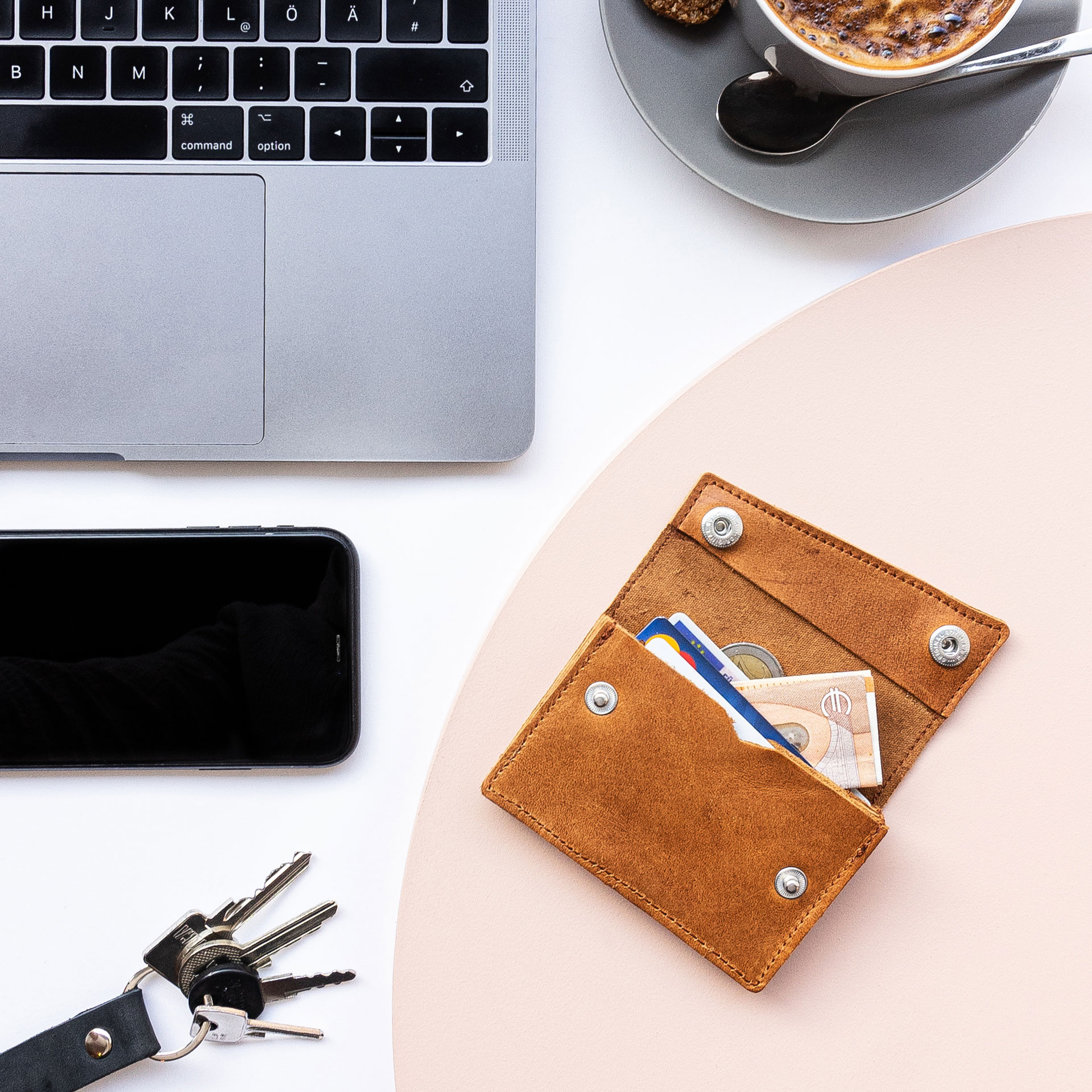 Portemonnaie ENO auf einem Tisch liegen im Größenvergleich mit einem Smartphne, Laptop, Kaffee und Schlüsselbund.