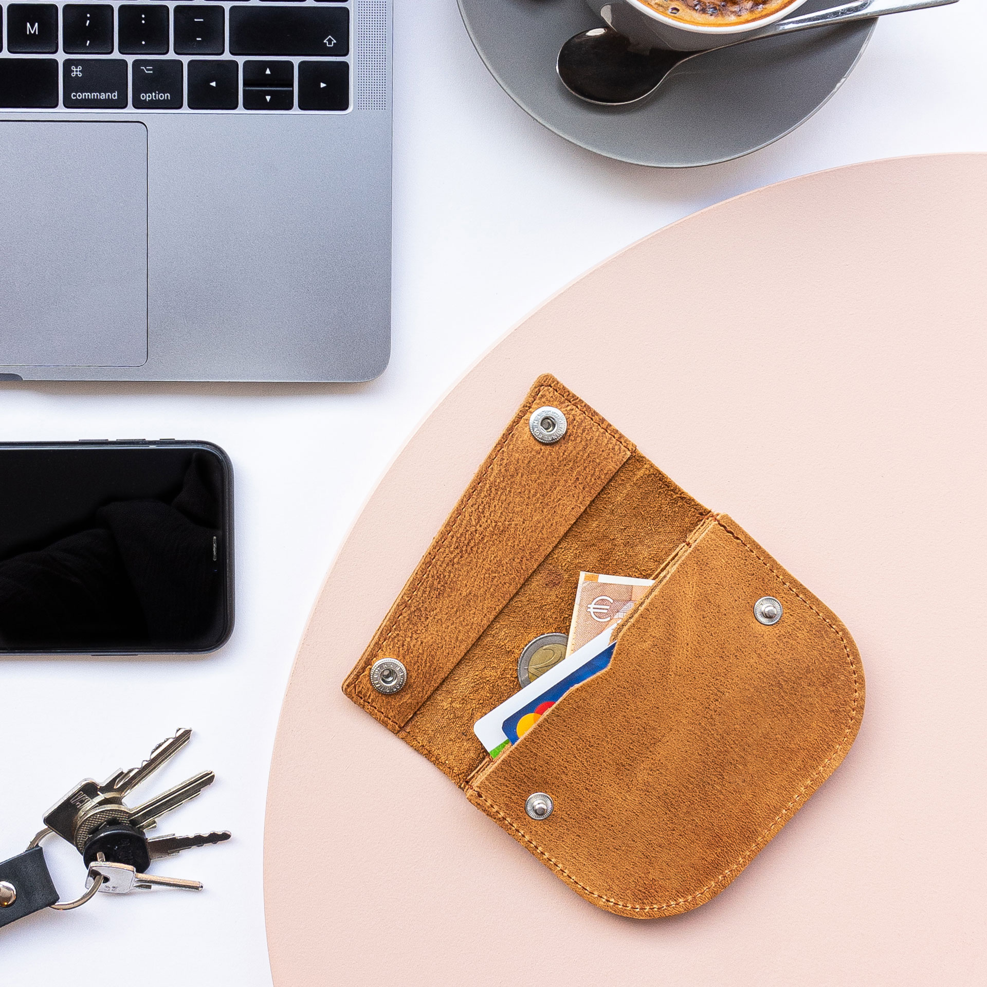Portemonnaie ENO auf einem Tisch liegen im Größenvergleich mit einem Smartphne, Laptop, Kaffee und Schlüsselbund.