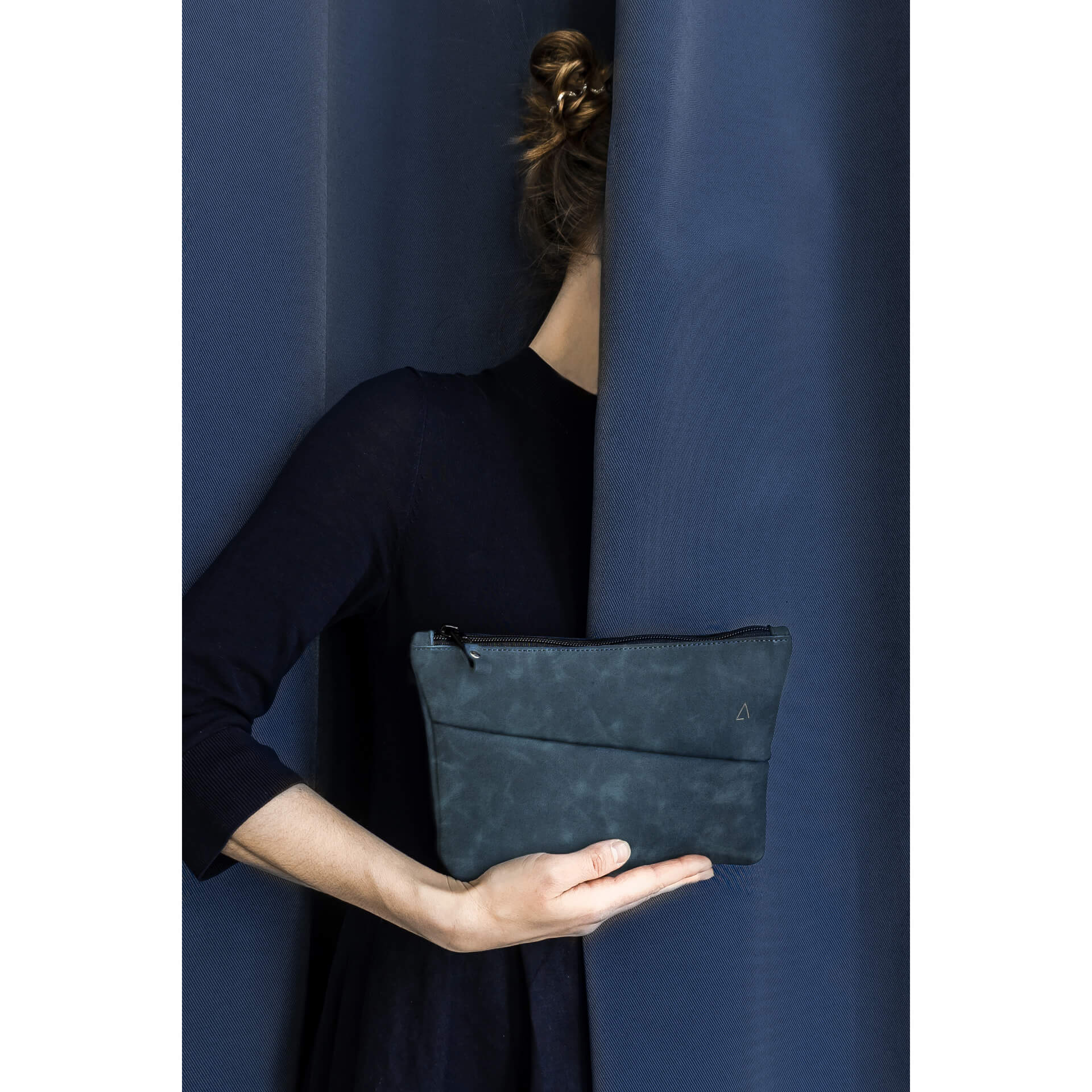 Utensilientasche Pouch FRA aus nachhaltigem Naturleder in Dunkelblau mit Logoprägung vor dunkelblauem Vorhang gehalten