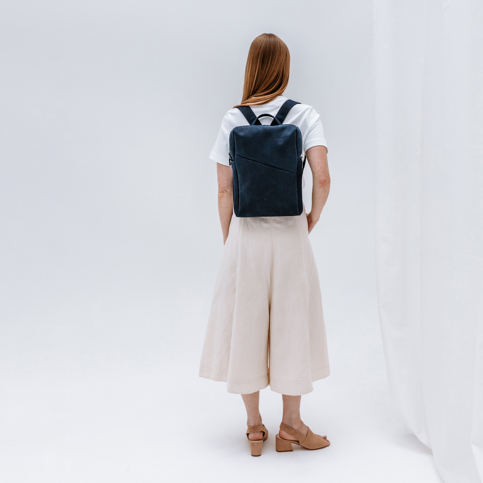 Model trägt Rucksack Neo Small in Dunkelblau aus nachhaltigem Naturleder.