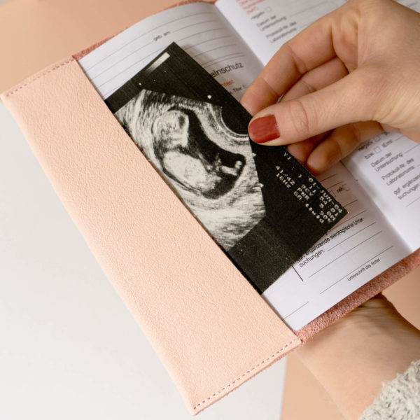 Frau legt Ultraschallbild in Mutterpasshülle EVE aus Naturleder in Rosa