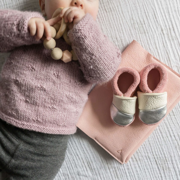 Mood Shot Baby liegt auf Decke neben U-Heftehülle EVE aus Naturleder in Rosa und konfigurierten Lauflernschuhen MOQ in Rosa, Creme und Silber