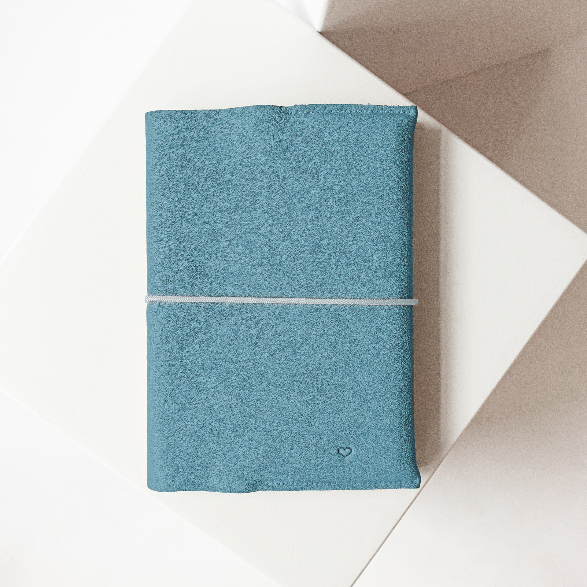 U-Hefthülle EVE aus nachhaltigem Naturleder in Hellblau mit schlichter Herz-Prägung und cremefarbenem Verschlussband